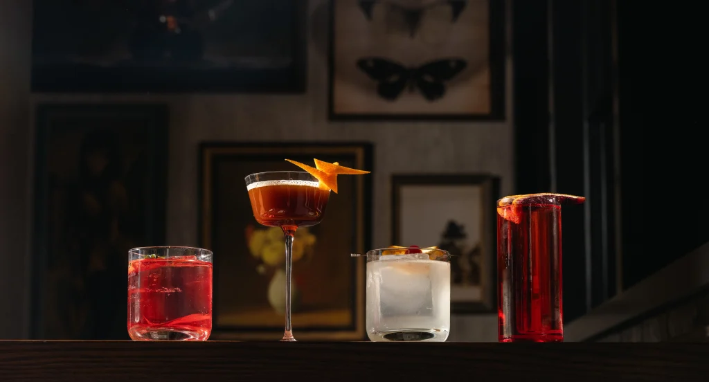Different cocktails from Alice lined up on a bar top captured with dramatic lighting